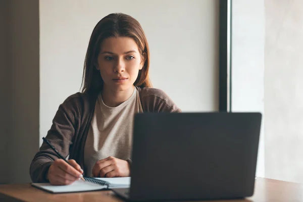 Jovem concentrada escrevendo notas enquanto escuta webinar grátis — Fotografia de Stock