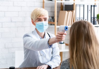 Hasta muayenesi. Koruyucu maskeli kadın doktor sıcaklığı ölçüyor