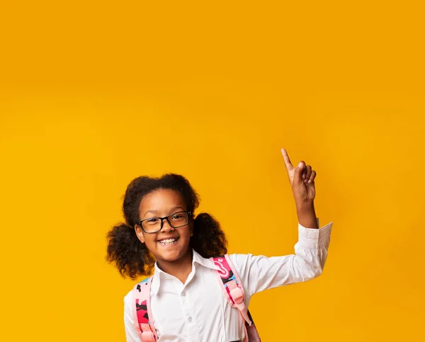 Feliz africana colegiala teniendo idea apuntando con el dedo hacia arriba, fondo amarillo — Foto de Stock