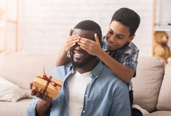 Feliz hijo felicitando a su padre afro, cubriendo los ojos y dando regalo — Foto de Stock