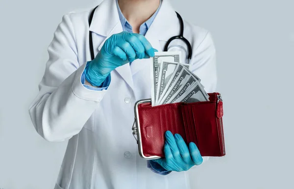 Doctor in white coat holds red purse with dollars in hands and takes money — Stock Photo, Image