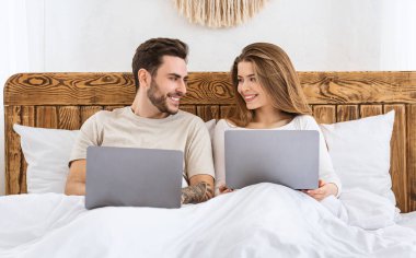 Akşamları online alışveriş. Yatakta dizüstü bilgisayarları olan kız ve erkek.