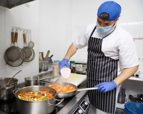 Uomo in maschera e guanti che cucina verdure fresche su piano cottura professionale — Foto Stock