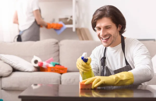 Limpieza doméstica. Hombre sonriente limpiando el polvo de la mesa en casa — Foto de Stock