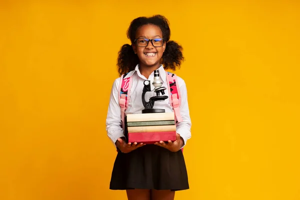 Gelukkig Afrikaans meisje met boeken en microscoop leren, gele achtergrond — Stockfoto