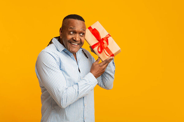 Curious mature african american man shaking present box