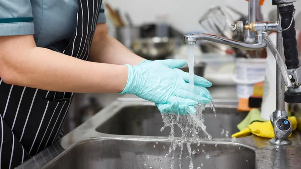 Mujer con guantes azules lavándose bien las manos bajo el agua — Foto de Stock