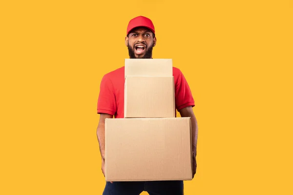 Hombre de mensajería sobrecargado de trabajo sosteniendo cajas de cartón de pie sobre fondo amarillo — Foto de Stock