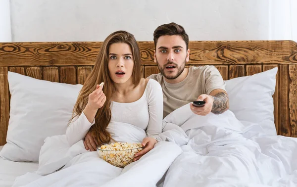 Filme no conceito de cama. Surpreendido marido e mulher assistindo tv — Fotografia de Stock