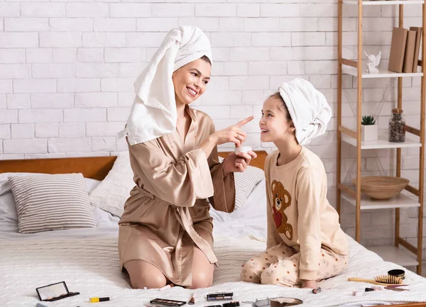 Salón de belleza hija madre. Chica feliz y su mamá en toallas de baño aplicando maquillaje en casa —  Fotos de Stock