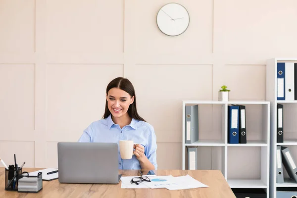 Podnikatelka pracující na notebooku s kávou těší práci v kanceláři — Stock fotografie