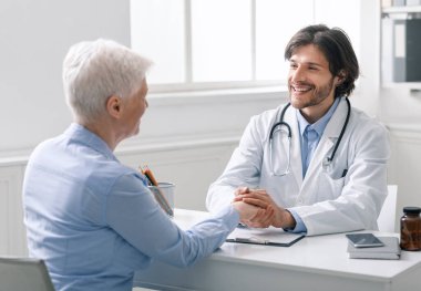 Bakıcı doktor, yaşlı kadının elini tutuyor.