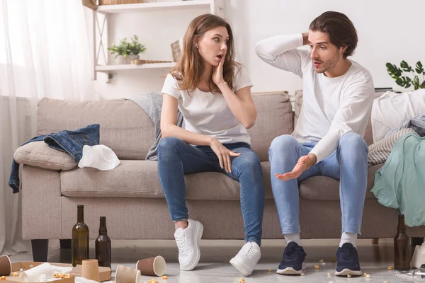 Chocado Millennial casal olhando para o seu apartamento bagunçado depois da festa — Fotografia de Stock