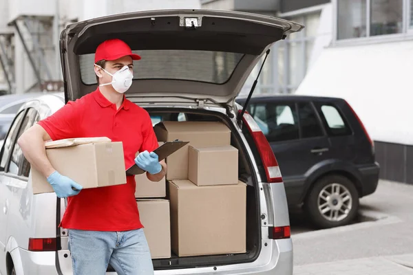 制服、保護マスクと手袋の宅配便は、小包と車のトランクの近くに立つ — ストック写真