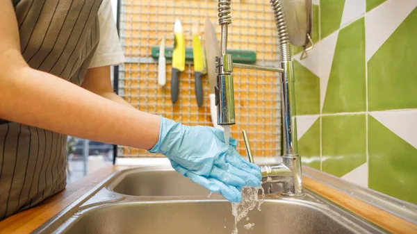 Mujer irreconocible con guantes lavándose las manos bajo el agua — Foto de Stock