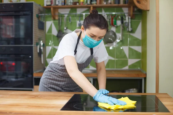 Donna in maschera e guanti disinfettante le superfici della cucina — Foto Stock