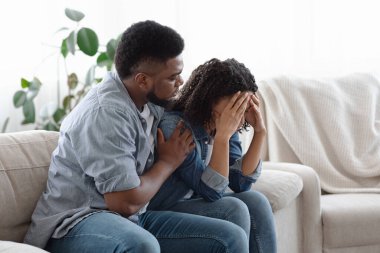 Bağımlı İlişki. Genç siyah adam depresyondaki kız arkadaşını evinde sakinleştiriyor.