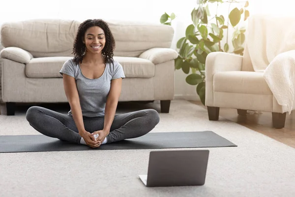 Domestic Yoga. Smiling African Woman Meditating At Home In Front Of Laptop