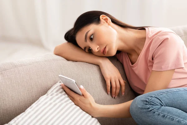 沮丧的女人坐在沙发上检查手机 — 图库照片