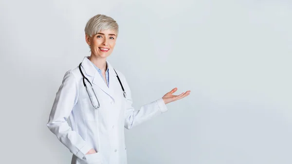 Kobieta zaprasza na spotkanie. Uśmiechnięty lekarz w białym płaszczu pokazuje gest powitania — Zdjęcie stockowe