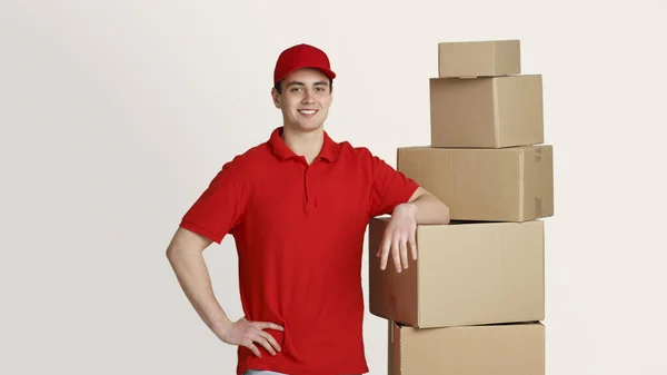 Mensajero sonriente se encuentra en el almacén de almacenamiento y pone la mano en cajas, estudio de tiro — Foto de Stock