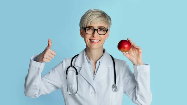 Een goed voedingsconcert. Vrouw arts gebaren teken uitstekend en het houden van appel — Stockfoto