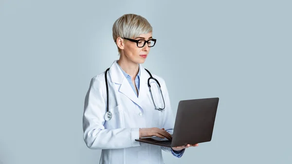 Nowoczesna koncepcja wizyty u lekarza. Kobieta lekarz w białym płaszczu i okulary pisząc historię choroby do laptopa — Zdjęcie stockowe