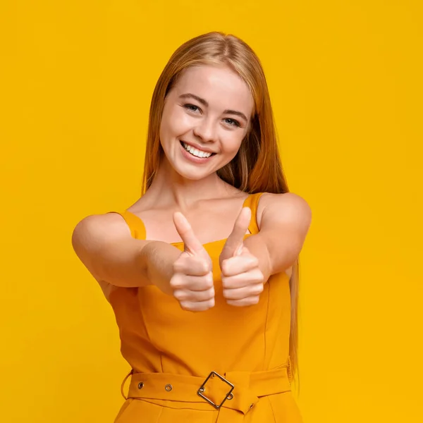Радісна дівчина-підліток жестикулює великі пальці вгору на камеру над жовтим тлом — стокове фото