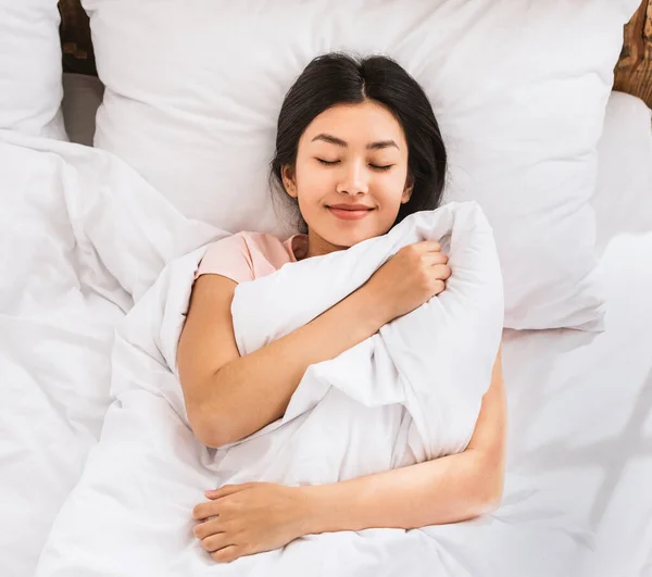 Asiático chica despertar en cama abrazando manta arriba vista —  Fotos de Stock