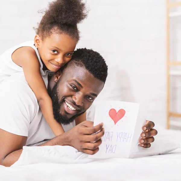 Afrikaner hält handgemachte Grußkarte in der Hand, Tochter umarmt ihn — Stockfoto
