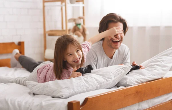 Menina brincalhão cobrindo seus olhos de pai enquanto joga videogame — Fotografia de Stock