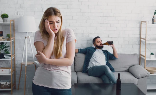 Mujer infeliz presiona su mano a la mejilla, el hombre ve la televisión y bebe cerveza de la botella en casa — Foto de Stock