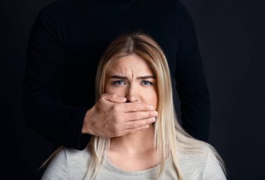 Erkek eli, arkasında siyah bir siluet olan ümitsiz, korkmuş bir kızın ağzı.