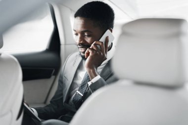 Otomobilde arka koltukta oturan iş adamı cep telefonuyla konuşuyor.