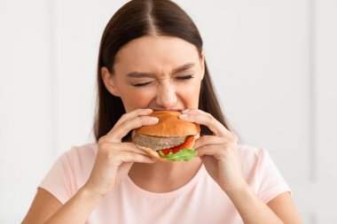 Burger yiyen kız evde fast food yiyor.