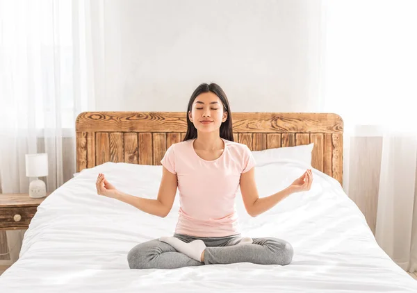 Mulher asiática meditando sentado na posição de lótus na cama interior — Fotografia de Stock