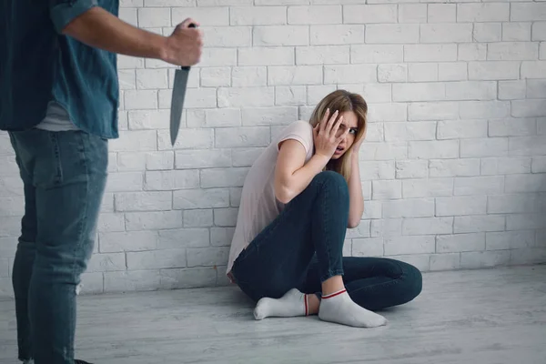 Mujer asustada sentada en el suelo, escondida del hombre, amenazándola con un cuchillo de cocina — Foto de Stock