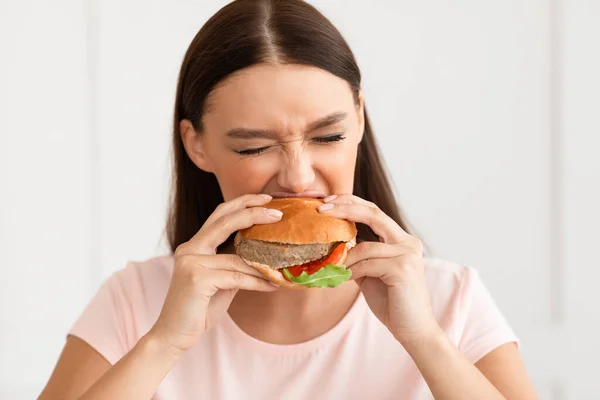 Menina comer hambúrguer desfrutando de fast food em casa — Fotografia de Stock