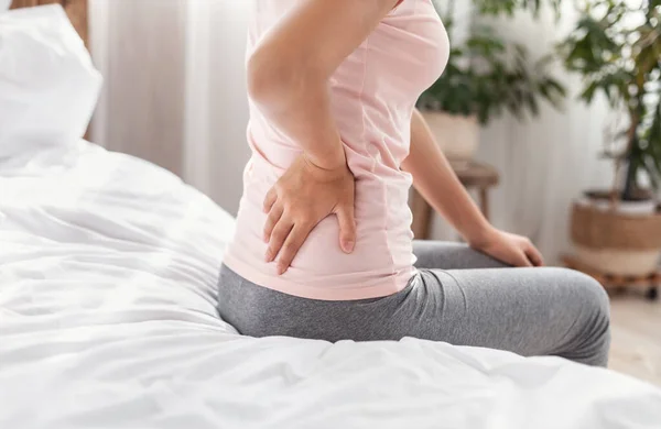 Onherkenbare dame aanraken terug lijden van pijn zittend op bed — Stockfoto