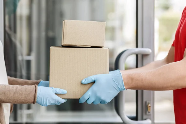 Ręce kuriera w rękawiczkach ochronnych dają pudełka klientowi przy drzwiach — Zdjęcie stockowe