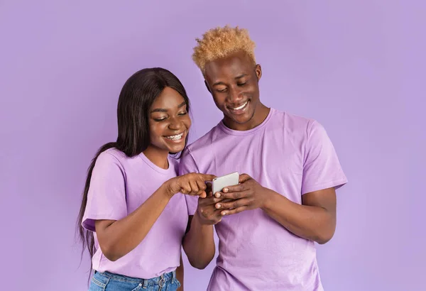 Alegre preto menina e cara usando celular juntos no violeta fundo — Fotografia de Stock