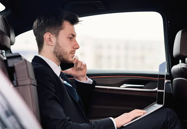 Jovem empresário falando no telefone no carro usando seu PC — Fotografia de Stock