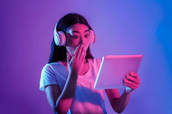 Surpris asiatique fille en gros écouteurs ferme sa bouche avec la main et regarde tablette — Photo