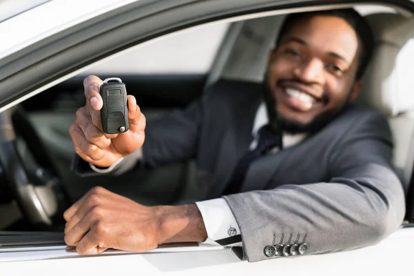 Чорний чоловік показує ключ автомобіля сидячи в авто, мала глибина — стокове фото
