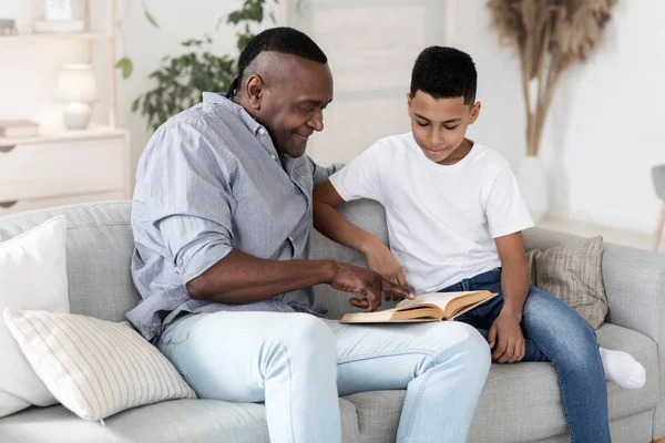 Family Education. Black Grandfather Reading Book With His Preteen Grandson At Home