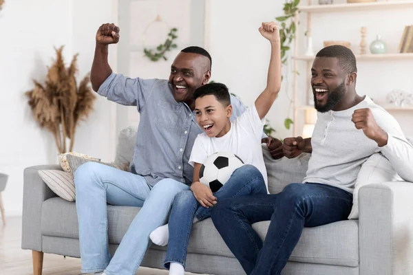 Emocionado abuelo negro, papá e hijo animando equipo de fútbol favorito en casa — Foto de Stock
