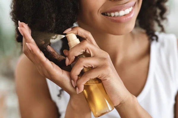 Trattamento delle estremità divise. Sorridente donna nera spruzzando olio essenziale sui capelli ricci — Foto Stock