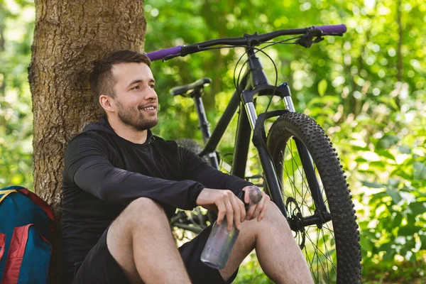 Portrait of happy cyclist resting under tree in forest