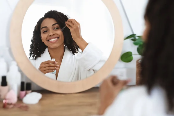 Bőrtáplálás. Gyönyörű fekete nő alkalmazása hidratáló szérum az arcon otthon — Stock Fotó