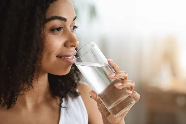 Liquido sano. Sorridente donna nera che beve acqua dal vetro e guarda lontano — Foto Stock